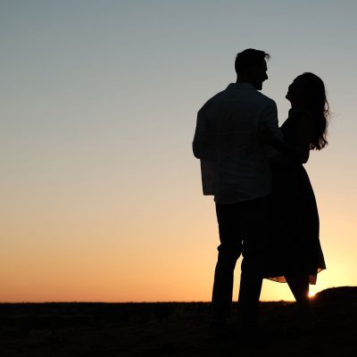Silhouette of couple at sunset standing on top of a dune and embracing.