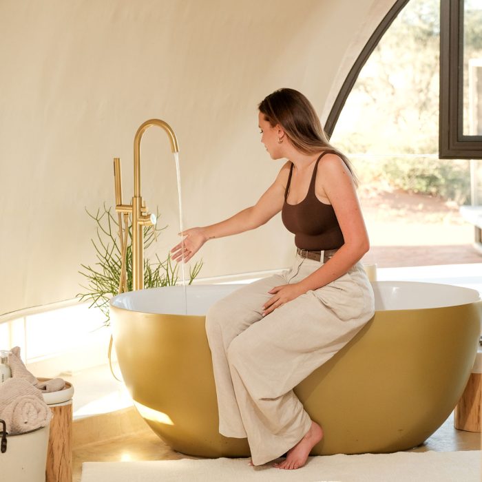Woman sitting on edge of golden bathtub in a luxurious bathroom.