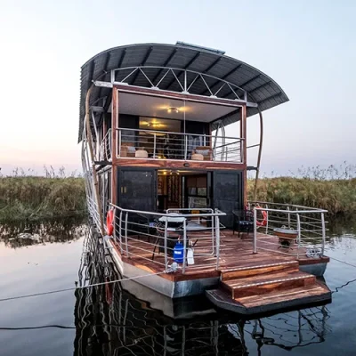 A two-story luxury safari vessel docked on a calm river.