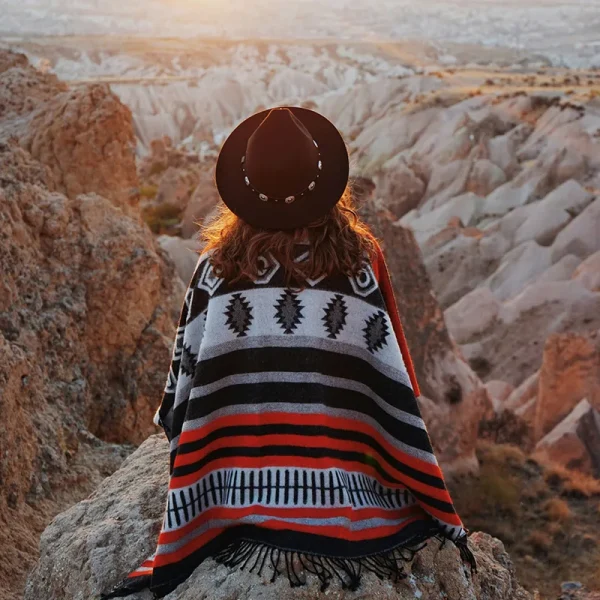 Hiker in a poncho at sunrise overlooking a vast, rugged canyon landscape
