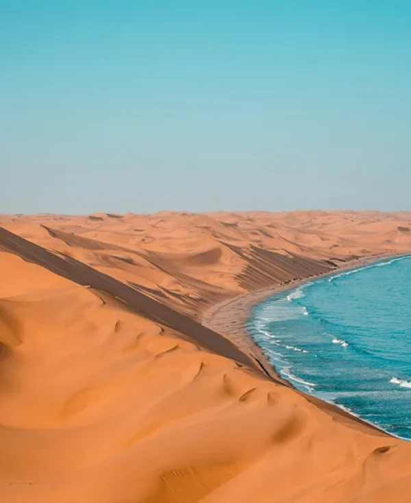 Towering orange sand dunes meeting the blue ocean waves near Swakopmund, Namibia Towering orange sand dunes meeting the blue ocean waves near Swakopmund, Namibia
